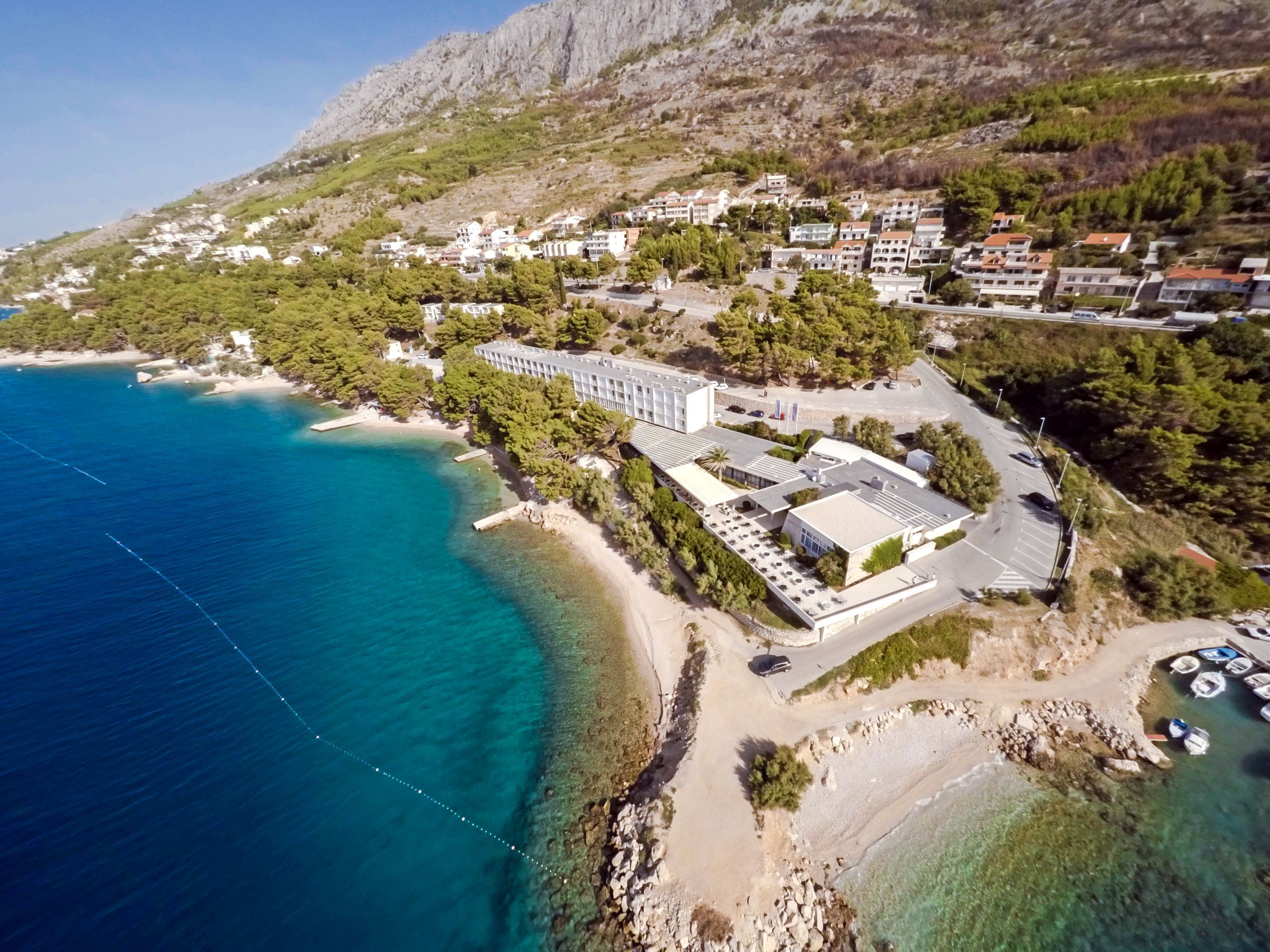 Vista aérea de un pueblo costero con edificios, una playa y aguas azules cristalinas.