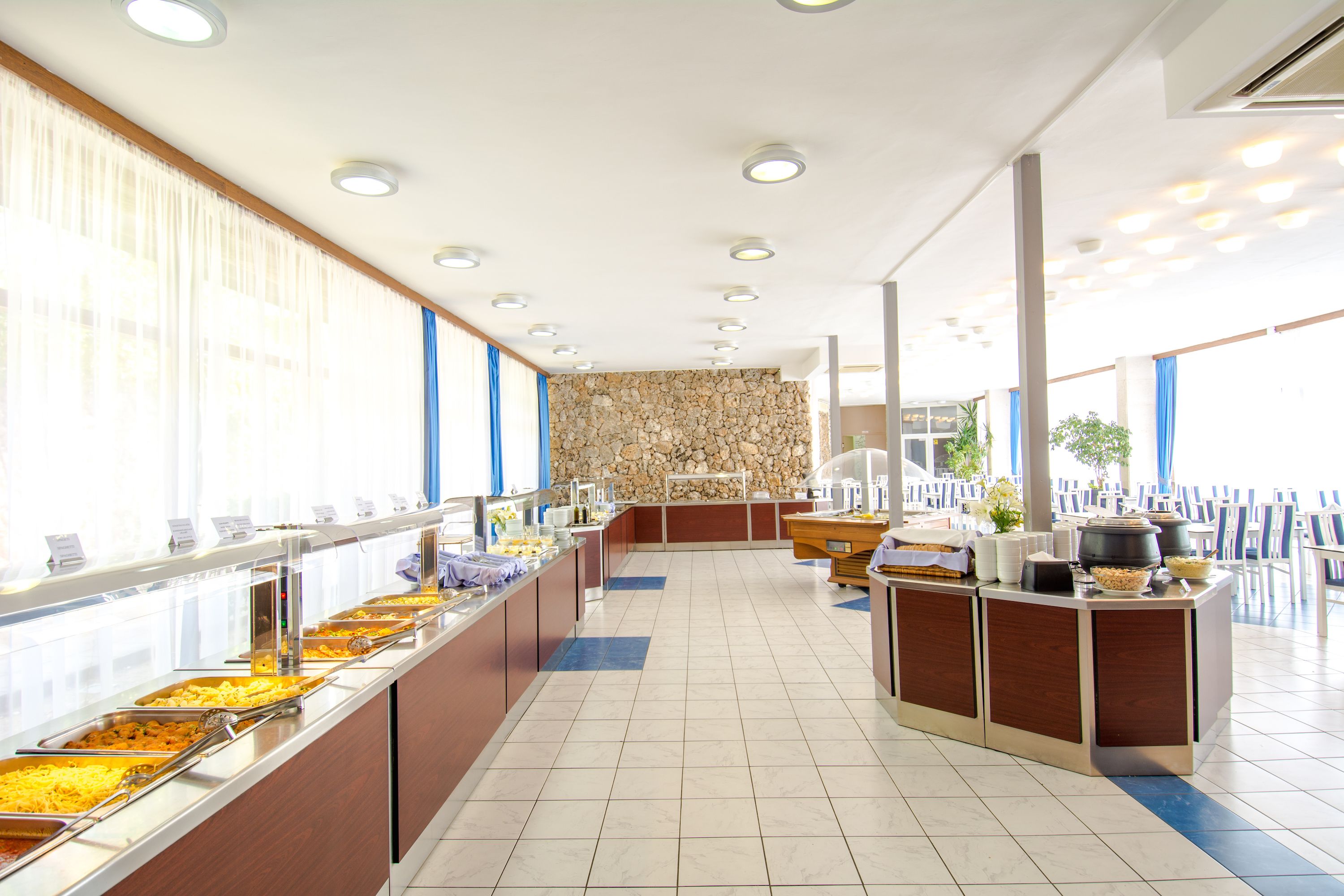 Ein Buffetbereich mit mehreren Speiseausgaben, einer Steinwand und einer Sitzgelegenheit mit Stühlen.
