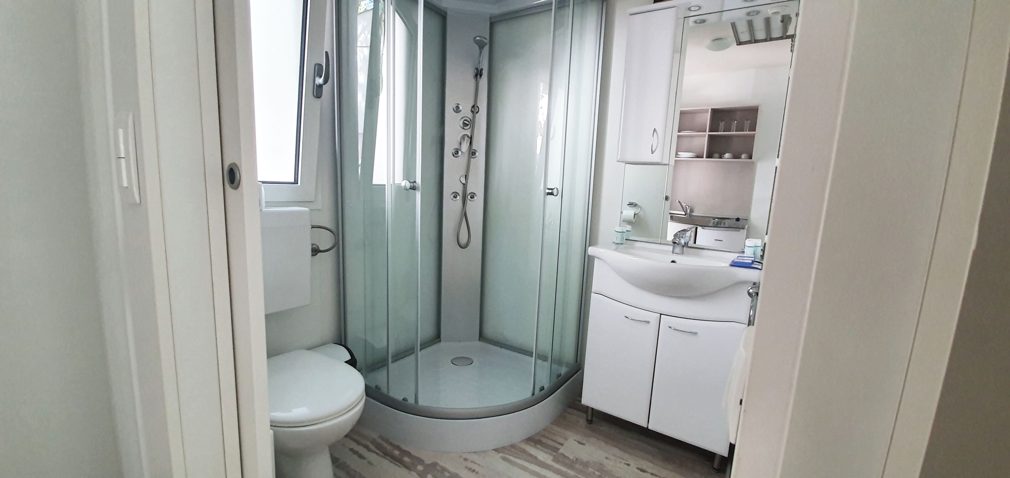 Une petite salle de bain dotée d’une douche à parois de verre, de toilettes et d’un lavabo avec des placards.