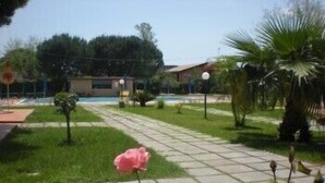 A paved pathway in a garden area with a pink flower in the foreground. - Villaggio Artemide (Giardini Naxos)