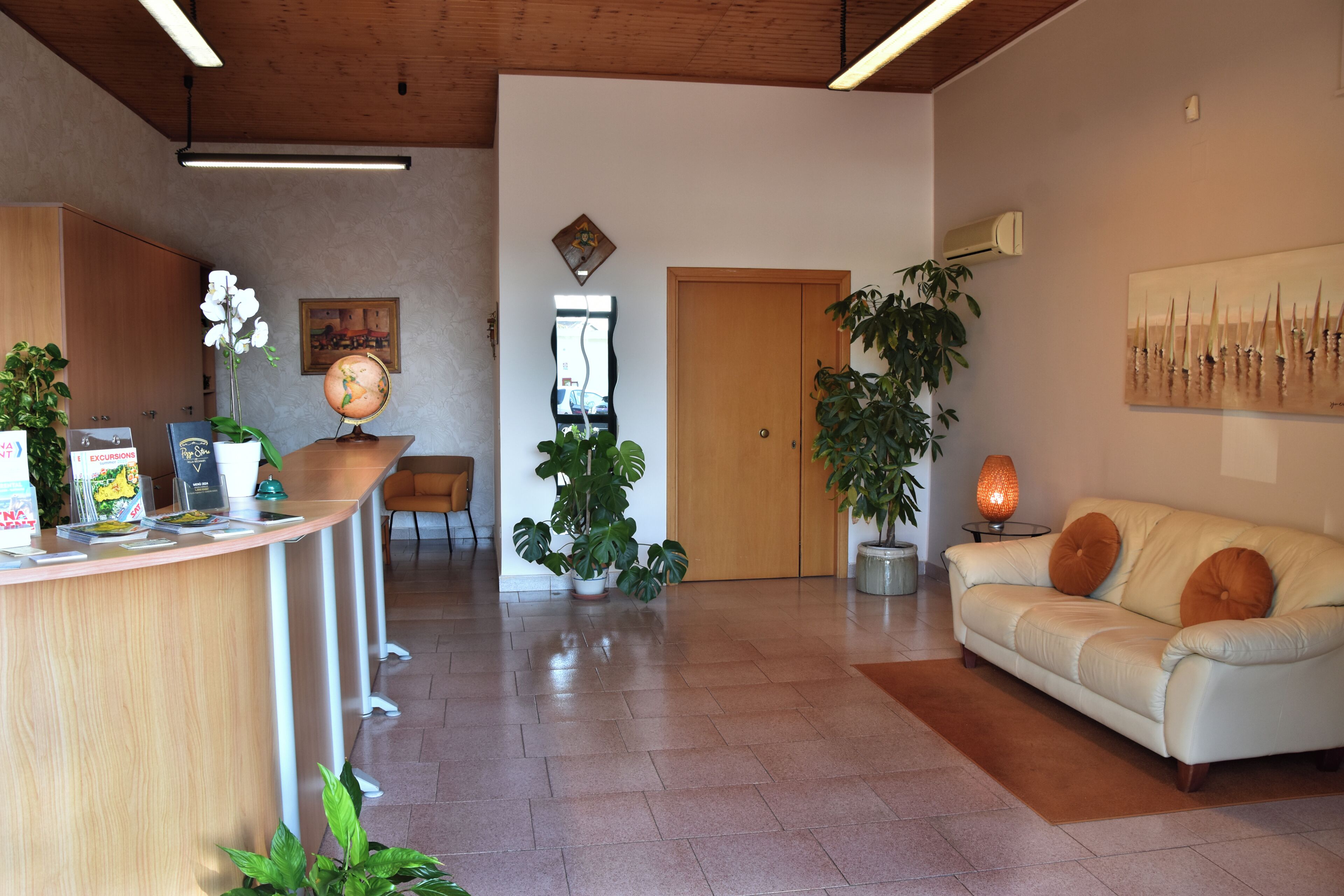 A spacious living area with a reception desk, a sofa, and various plants.