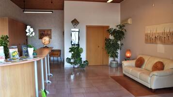 A spacious living area with a reception desk, a sofa, and various plants.