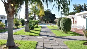 Un camino pavimentado que conduce a un área de piscina con palmeras y follaje.