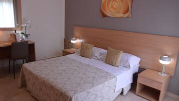 A hotel room with a bed, two bedside tables, a desk, a chair, and a wall-mounted painting.
