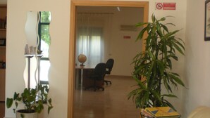 A living room with a beige sofa, a potted plant, and a wooden door leading to another room. - Villaggio Artemide (Giardini Naxos)