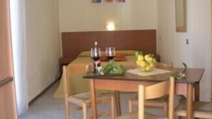 A small dining area with a table set for two, a bed in the background, and a wall-mounted mirror. - Villaggio Artemide (Giardini Naxos)