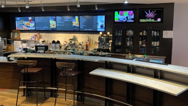 A bar area with a long counter, stools, and a menu display. - Courtyard by Marriott Oklahoma City North/Quail Springs (Oklahoma City)