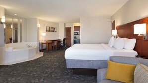 A hotel room with a large bed, a separate sitting area with a desk and chair, a bathroom with a bathtub, and a kitchenette. - Courtyard by Marriott Oklahoma City North/Quail Springs (Oklahoma City)