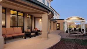 A hotel exterior with outdoor seating, large windows, and a covered area with tables and chairs. - Courtyard by Marriott Oklahoma City North/Quail Springs (Oklahoma City)