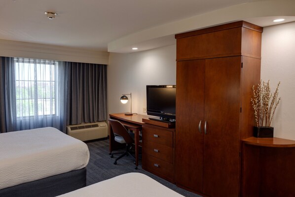 Habitación de hotel con dos camas, un escritorio con computadora, televisor y armario.