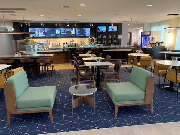 A modern restaurant with a bar area, multiple seating options including booths and tables, and a digital menu display.