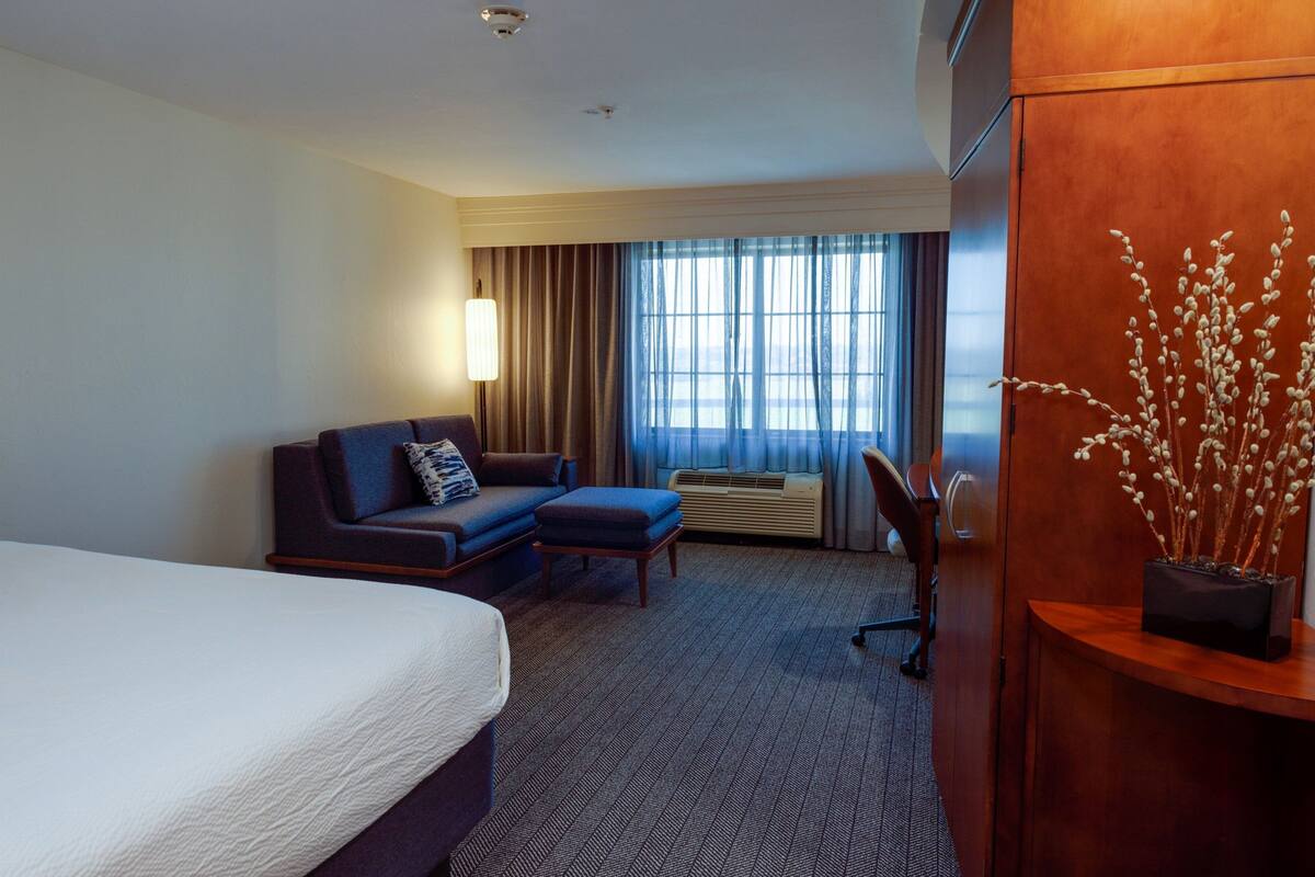 Une chambre d’hôtel avec un lit, un canapé, un bureau et une fenêtre avec des rideaux.