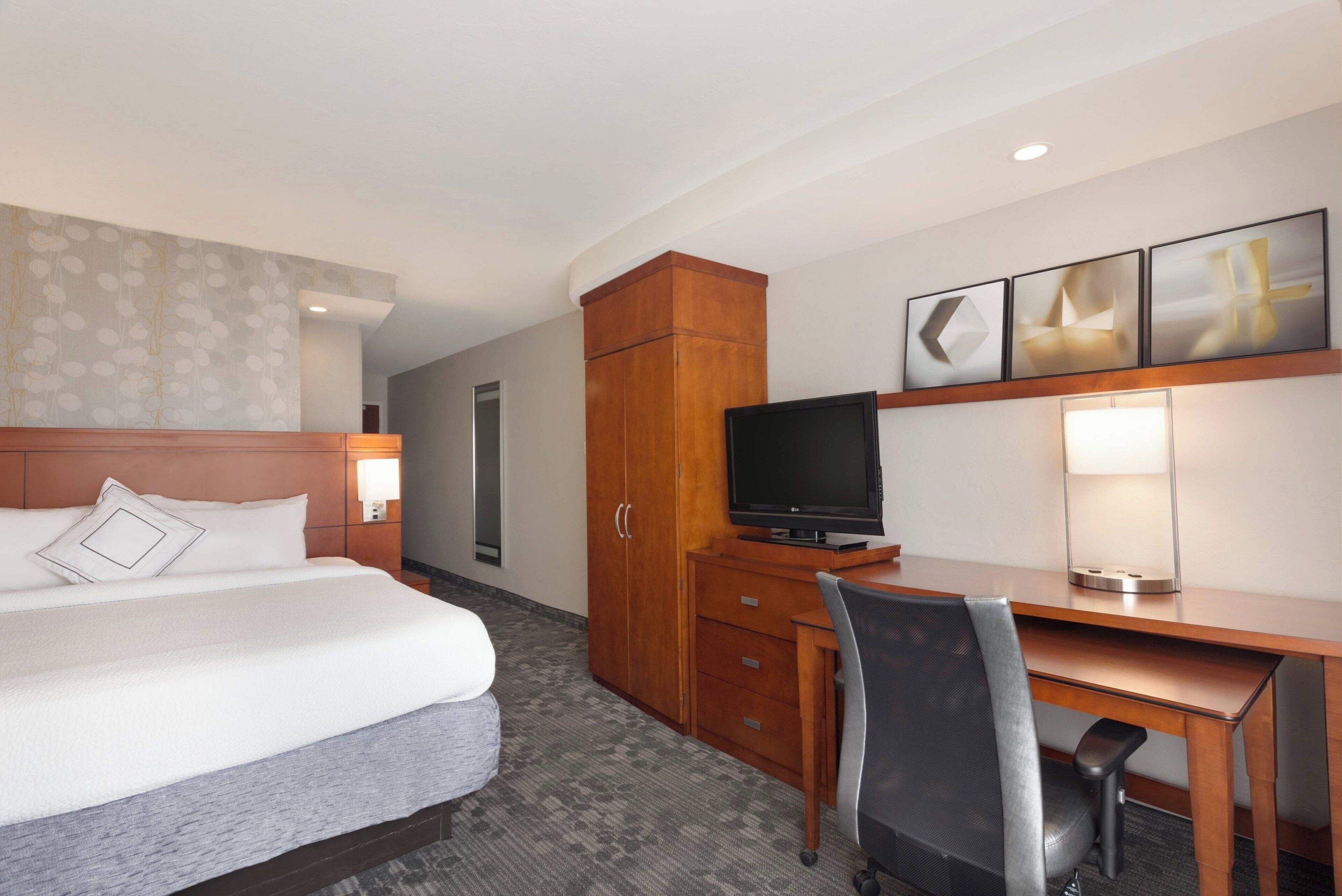 Une chambre d’hôtel équipée d’un lit, d’un bureau, d’une télévision, d’une armoire et d’une lampe fixée au mur.