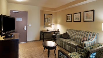 Une chambre d’hôtel avec une télévision posée sur un bureau, un canapé, une petite table et une porte avec une pancarte.