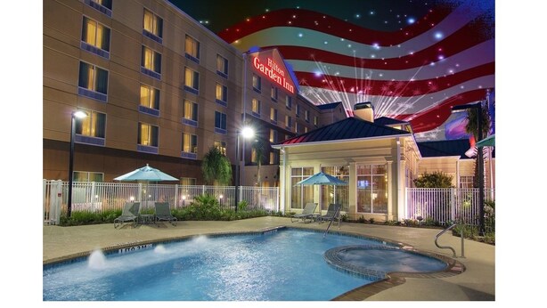 A hotel pool area with a pool, lounge chairs, and umbrellas. - Hilton Garden Inn Houston-Pearland (Pearland)