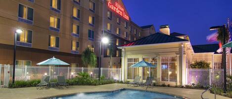 A hotel with a swimming pool, lounge chairs, and umbrellas.