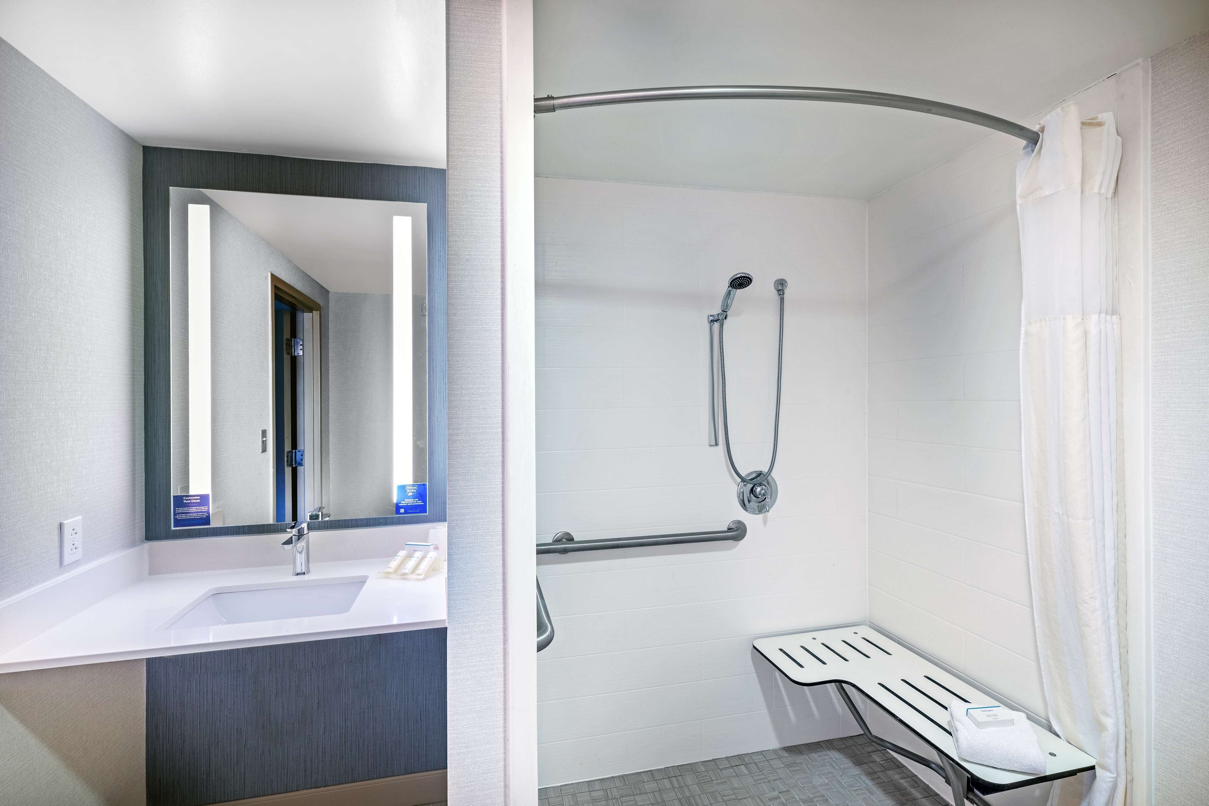 A bathroom with a white sink, mirror, and shower area with a bench.