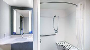 A bathroom with a white sink, mirror, and shower area with a bench.
