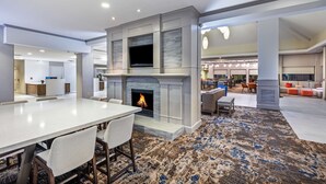 A modern hotel lobby with a fireplace, a dining area, and a seating area with a carpeted floor. - Hilton Garden Inn Houston/Sugar Land (Sugar Land)
