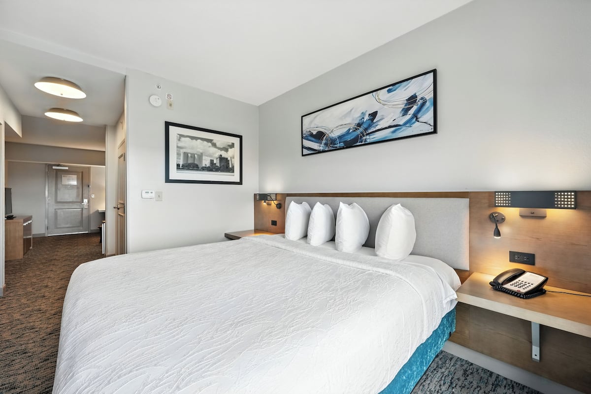 Ein Hotelzimmer mit einem großen Bett, einem Nachttisch mit Telefon, einer Wandleuchte und einem gerahmten Bild über dem Bett.