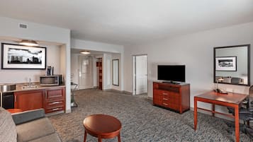 A hotel room with a kitchenette, a flat-screen TV, a wooden dining table, and a sofa.