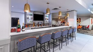 A modern bar area with a long counter, multiple bar stools, and pendant lighting. - Hilton Garden Inn Houston/Sugar Land (Sugar Land)
