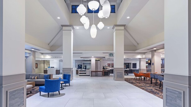 A spacious lobby with a central seating area, a reception desk, and a kitchen in the background. - Hilton Garden Inn Houston/Sugar Land (Sugar Land)