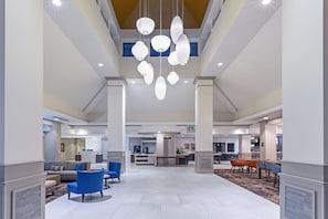 A spacious lobby with a central seating area, a reception desk, and a kitchen in the background. - Hilton Garden Inn Houston/Sugar Land (Sugar Land)