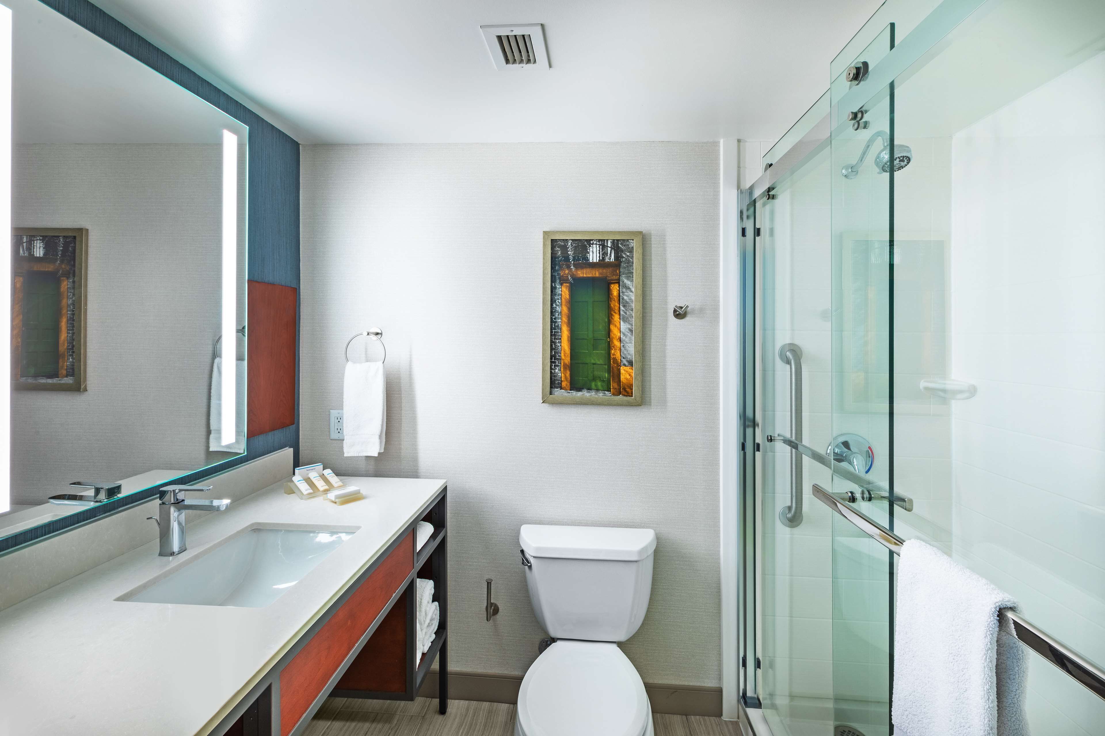 Een moderne badkamer met een grote spiegel, een wastafel, toilet en een douchecabine met glazen wanden.