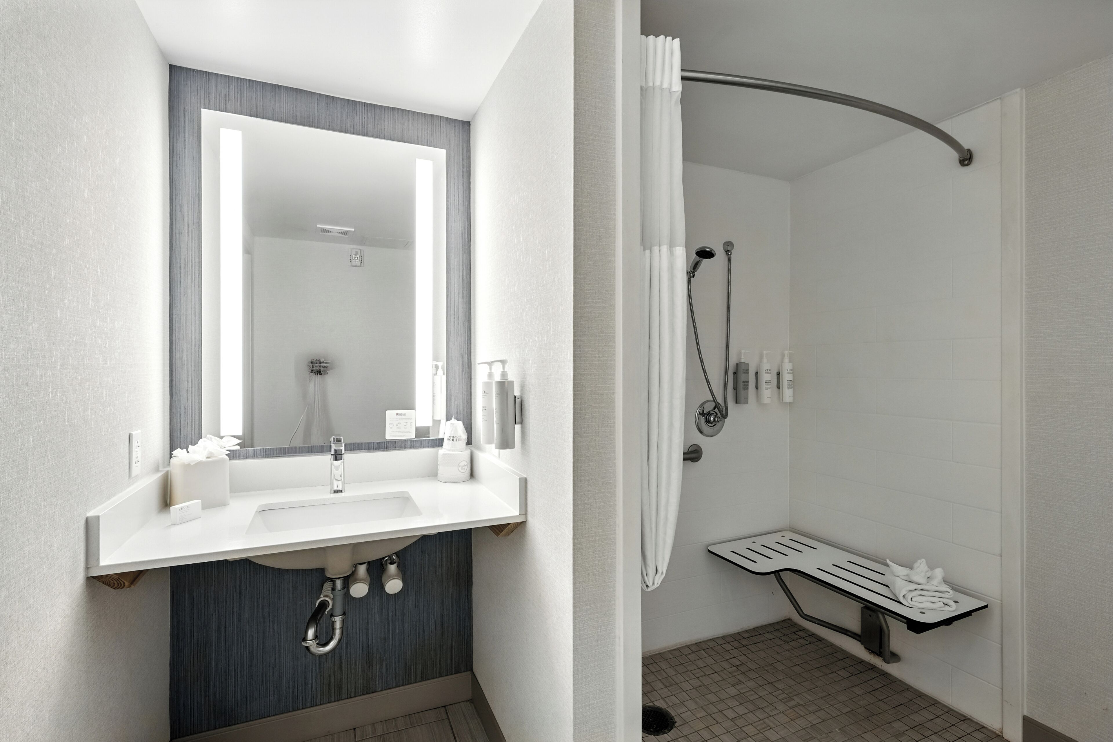 Un baño moderno con lavabo, espejo, ducha y toallero.
