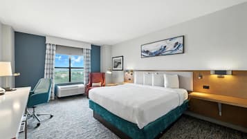 A hotel room with a bed, desk, chair, and a large window with a view.