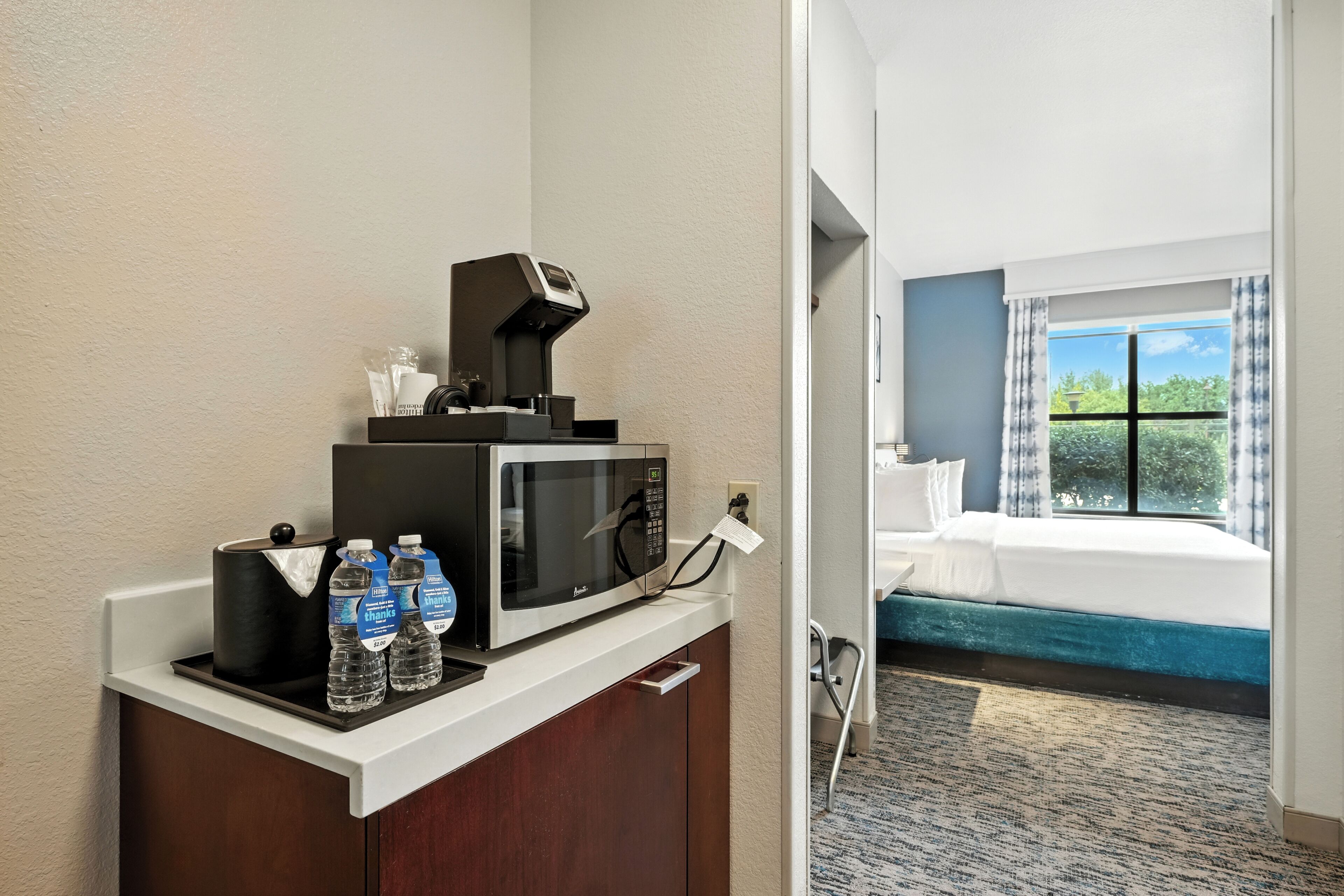 A hotel room with a kitchenette, a bed with a view, and a bathroom with a shower.