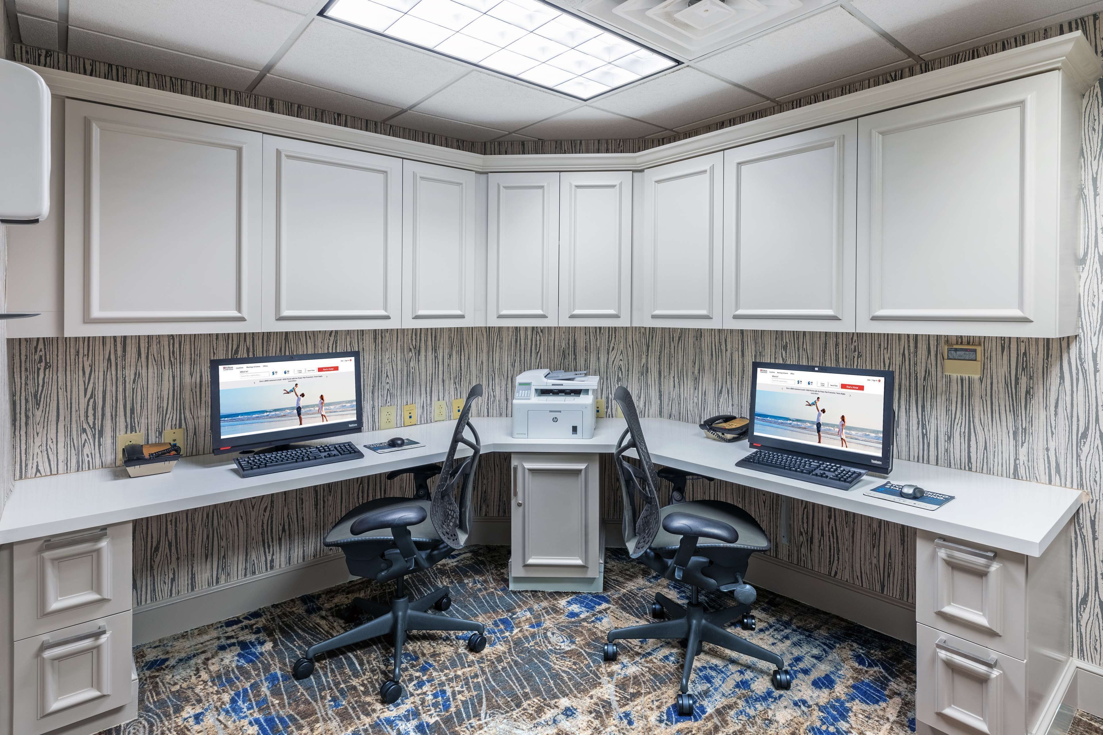 Ein Eckbüro mit zwei Schreibtischen, jeweils mit Computer, Stühlen und einem Drucker.