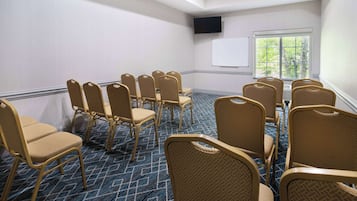 A conference room with rows of beige chairs, a whiteboard, and a large window with a view of trees.