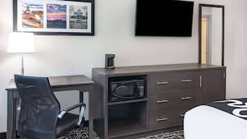 A hotel room with a desk, chair, microwave, dresser, and a bed.