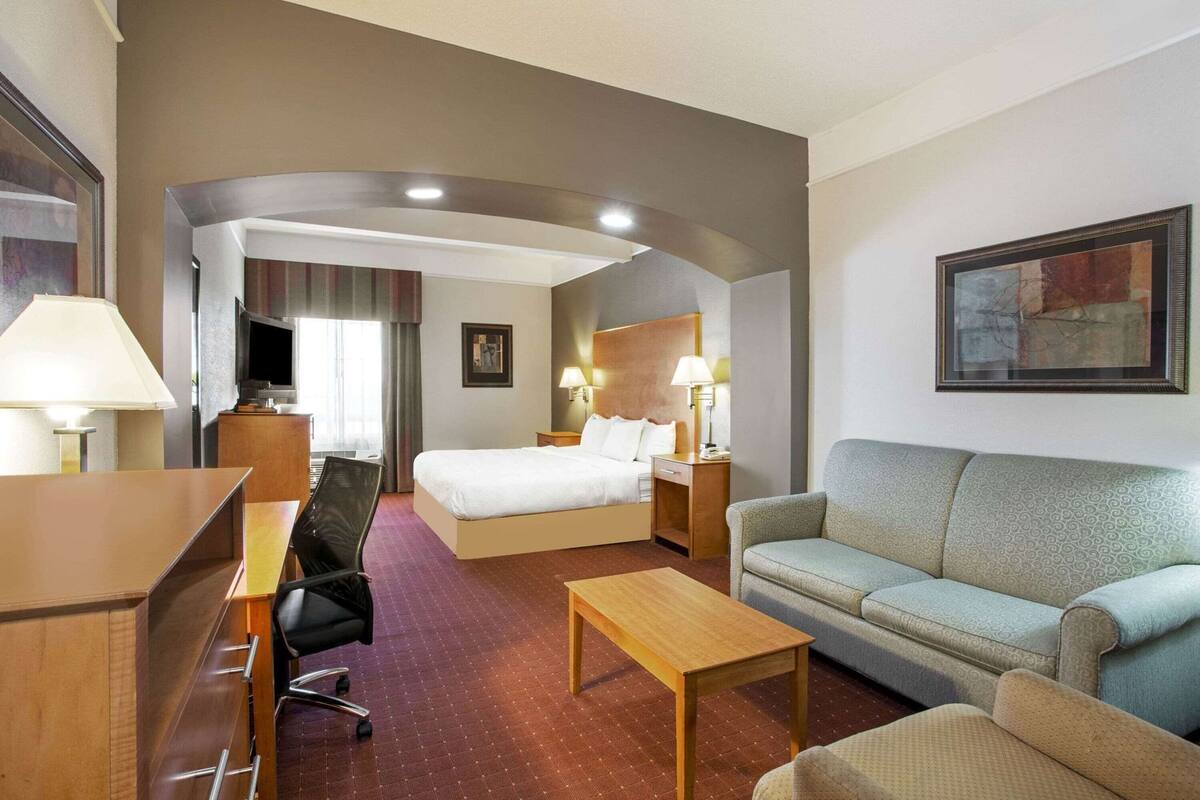 A hotel room with a bed, a sofa, a desk, and a TV.