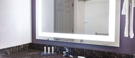 Un baño con un espejo grande, un lavamanos y un perchero para toallas.