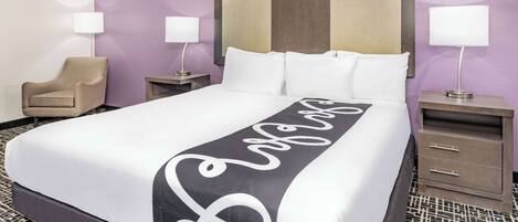 A neatly made bed with a black and white decorative runner, two bedside tables with lamps, a chair, and a headboard with a mirror.