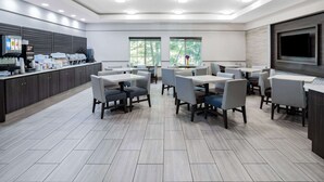 A modern dining area with tables and chairs, a coffee station, and a TV mounted on the wall.