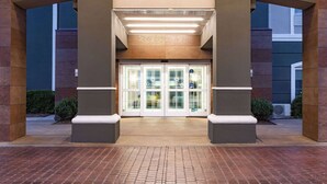 A hotel entrance with a glass door, a covered walkway, and a brick-paved area. - La Quinta Inn & Suites by Wyndham Norfolk (Norfolk)