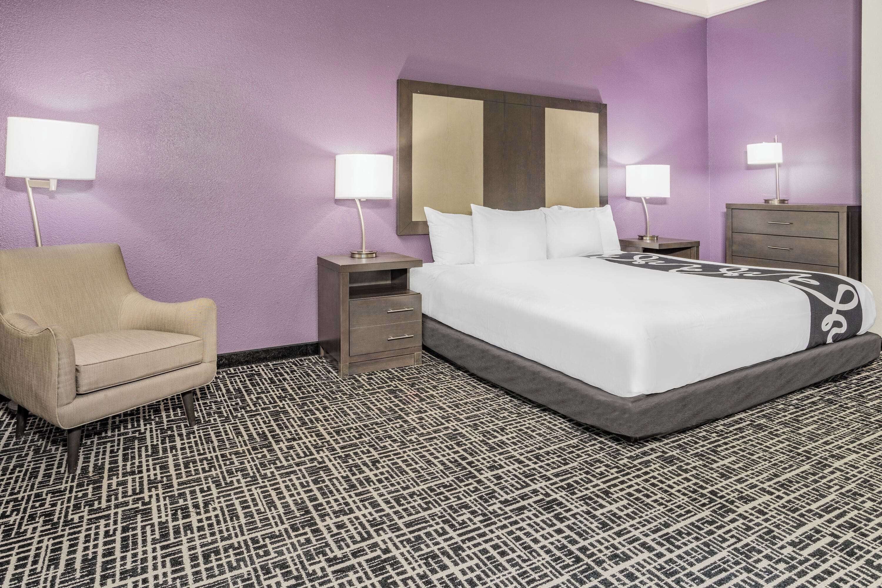 A hotel room with a large bed, two bedside tables with lamps, a chair, and a patterned carpet.
