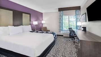 Habitación de hotel con una cama grande, un escritorio, una silla, un televisor y una ventana con cortinas.