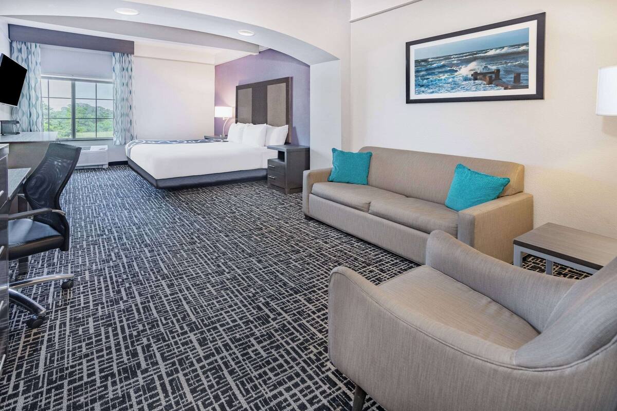 A hotel room with a bed, a desk, a chair, a sofa, and a TV.