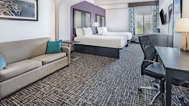 A hotel room with a bed, a desk, a chair, a sofa, and a large window with curtains.