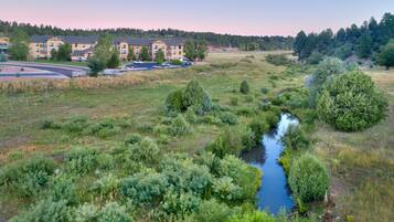 A residential area with a river, surrounded by greenery and a multi-story building with a parking lot.