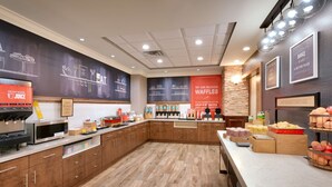 A breakfast area with a coffee machine, waffle station, and various food items.