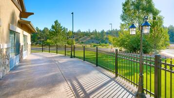 A paved walkway with a metal fence and street lamps, leading to a building with stone and stucco exterior.