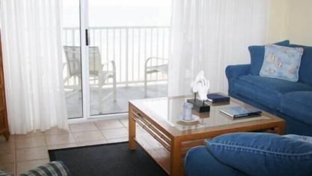 A living room with a glass door leading to a balcony, a blue sofa, a wooden coffee table, and a striped armchair.