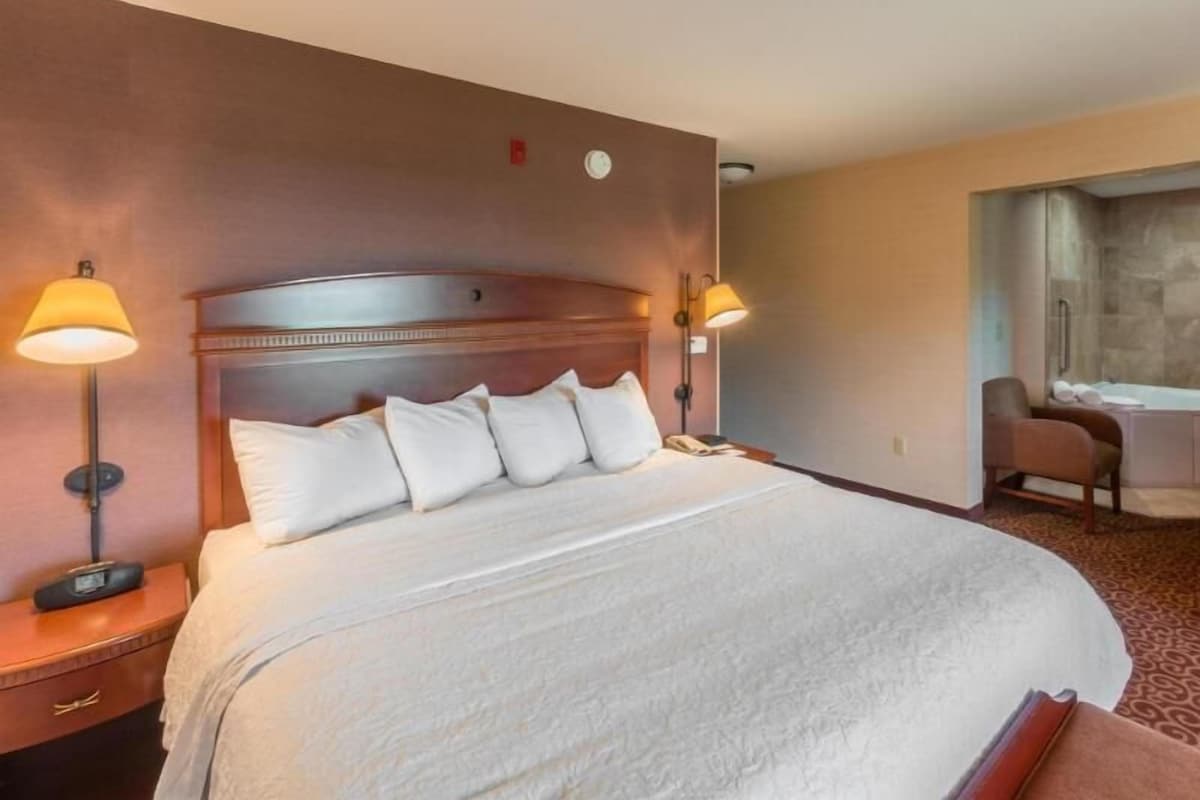 A hotel room with a large bed, bedside lamps, a desk, and a bathroom with a bathtub.