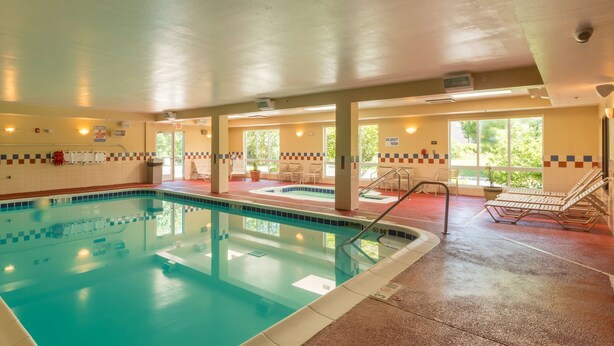 A swimming pool with a tiled deck, benches, and a covered area with windows. - Hampton Inn Goshen (Goshen)